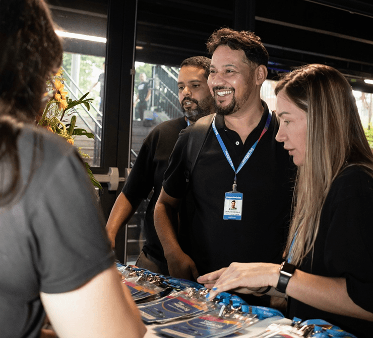 Participantes do evento Top Magalog interagindo em uma mesa de credenciamento, com crachás dispostos sobre a superfície.